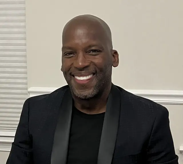 Albert Delon Reed Jr., smiling, in a black jacket