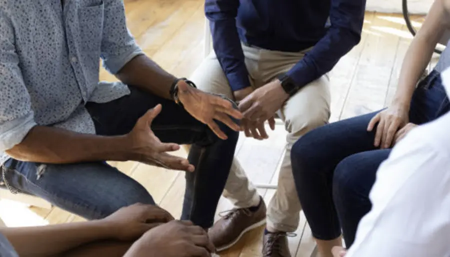 Group members seated in a circle, talking and gesturing during an in-person session
