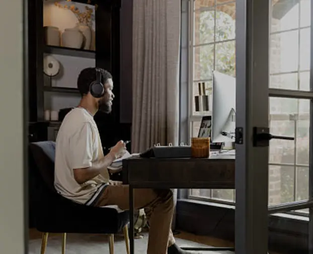 A man wearing headphones taking notes during a virtual session at his home desk